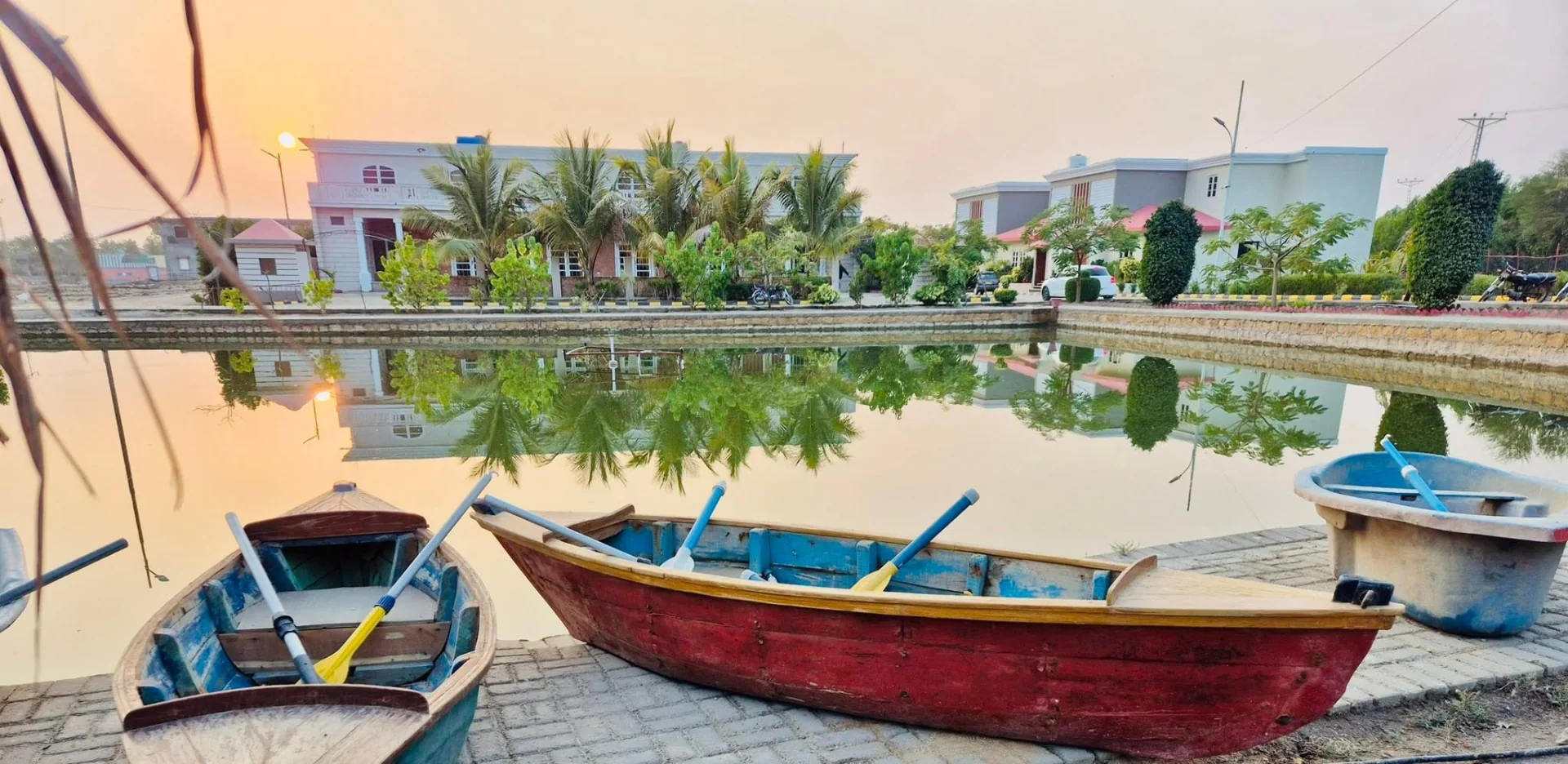 Wooden rowing boats resting beside the resort lake at sunset with buildings reflected in still water