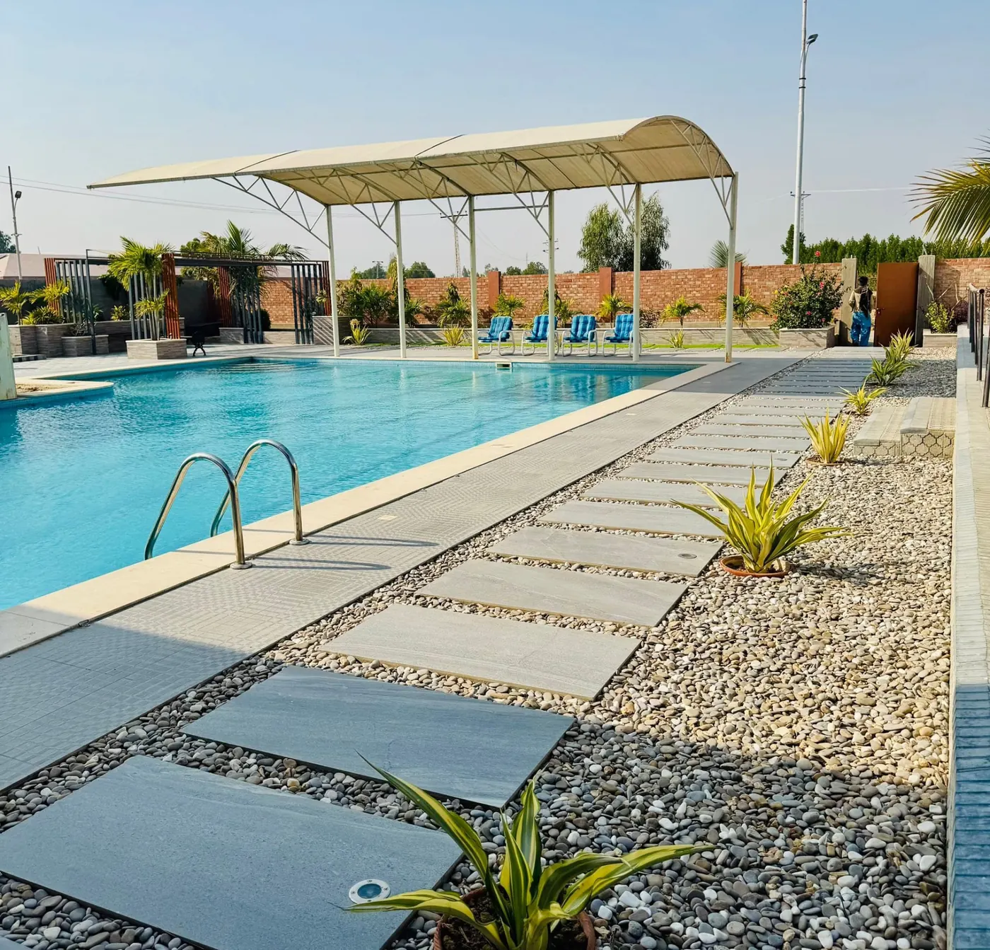 Swimming pool with a shaded canopy, loungers and pebble walkway